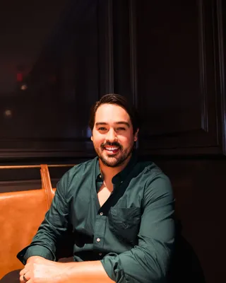 Mauri Villaseñor smiling, seated at a table in a leather booth against dark wood panels