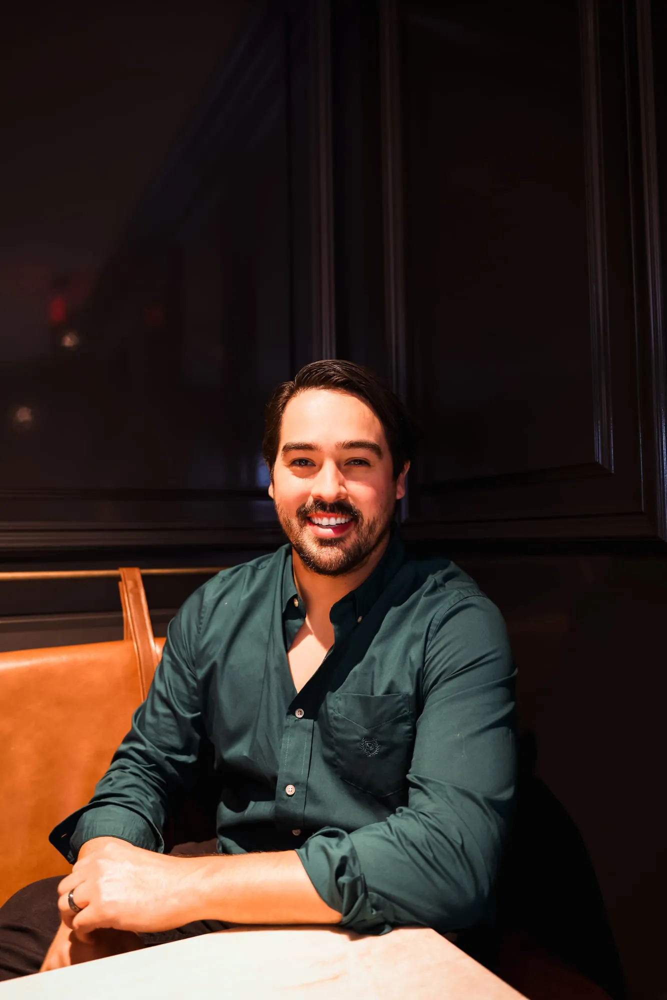 Mauri Villaseñor smiling, seated at a table in a leather booth against dark wood panels